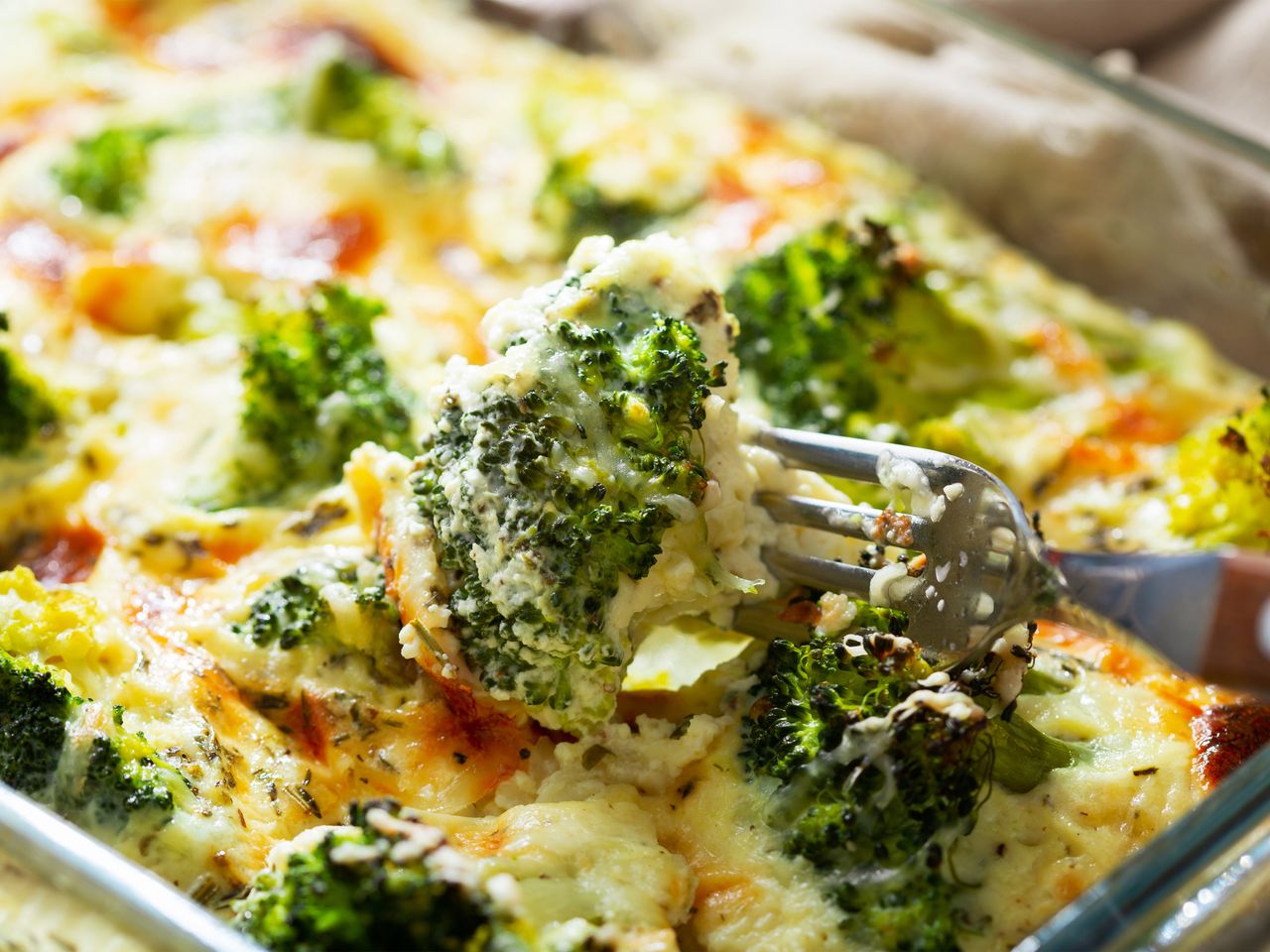 A fork digging into a cheesy looking creamy baked broccoli casserole