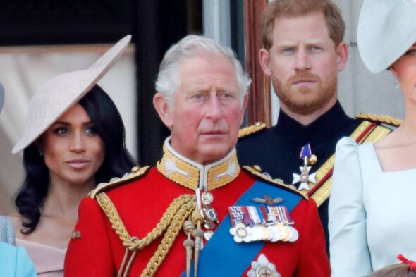 An adult male dressed in a royal military uniform stands between two other individuals, one wearing a hat and the other in forma