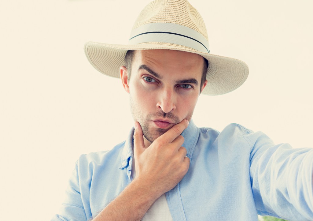Selfie of narcissistic man in hat, attractive man uses a mobile phone outdoors, portrait, toned