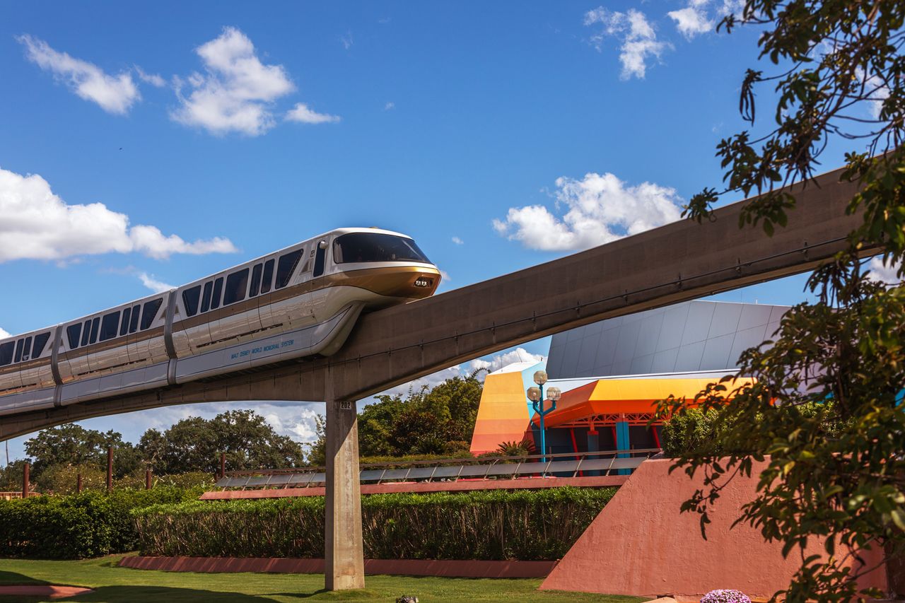 Monorail traveling on elevated tracks near a modern building and greenery