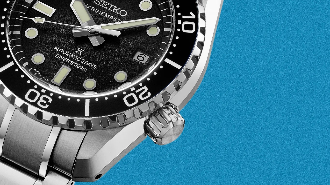 Close-up of a Seiko Marinemaster automatic diver's watch with a black dial and stainless steel bracelet on a blue background.