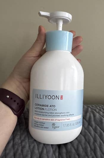 Person holding a bottle of Illiyoon Ceramide Ato Lotion, labeled for dry and sensitive skin, on a textured surface