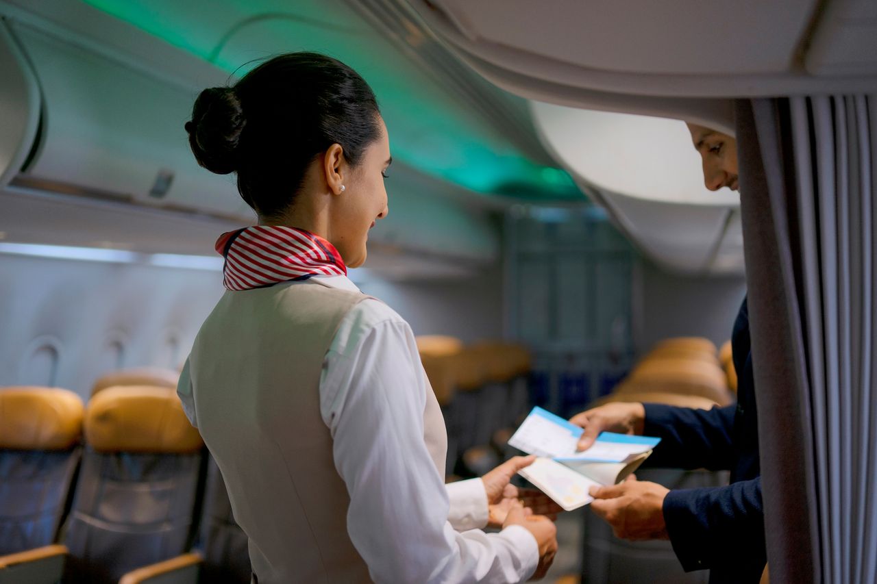 Flight attendant hands boarding passes to a passenger in an airplane cabin