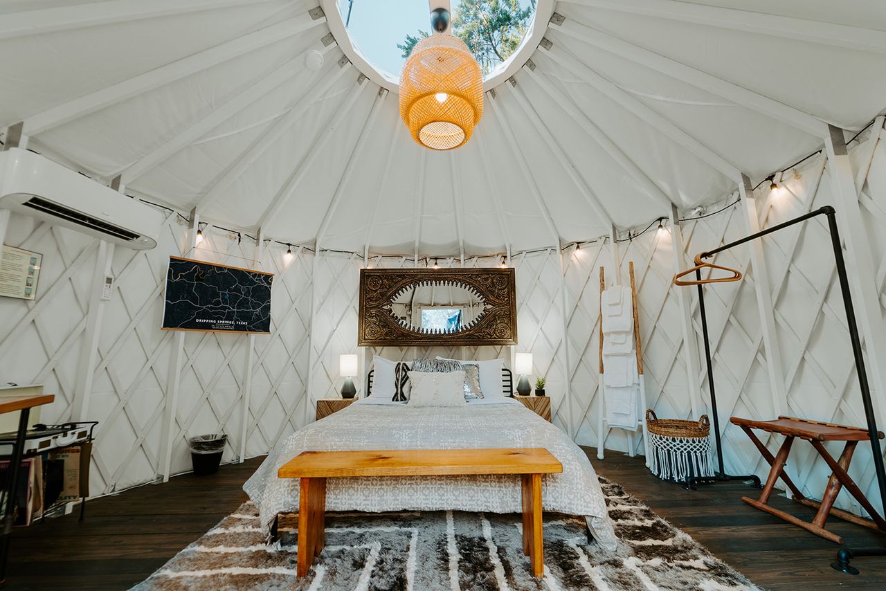 Interior view of a yurt with a bed and rustic decor including wooden furniture and a pendant light