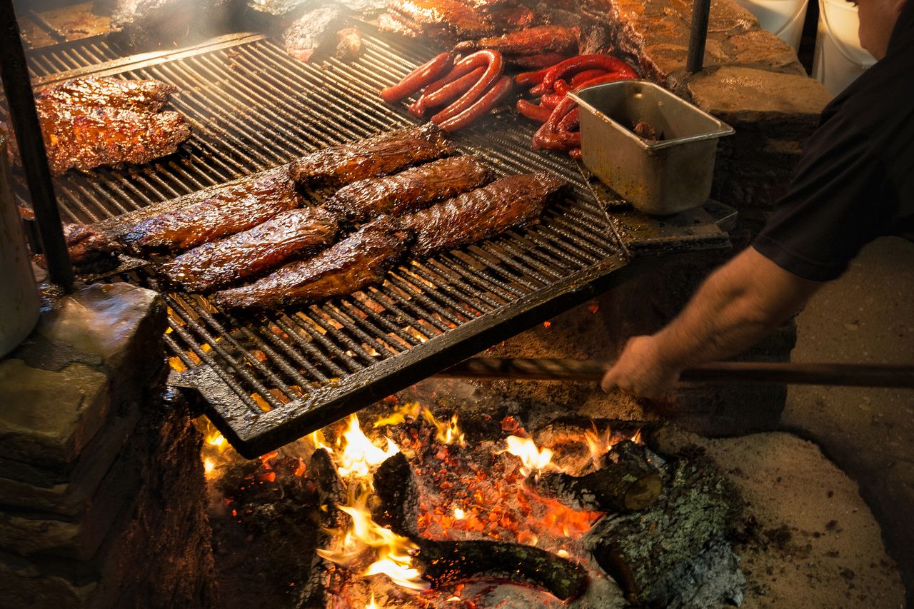 Barbecue being cooked on a grill over an open flame showing ribs sausages and other meat highlighting an outdoor cooking setup