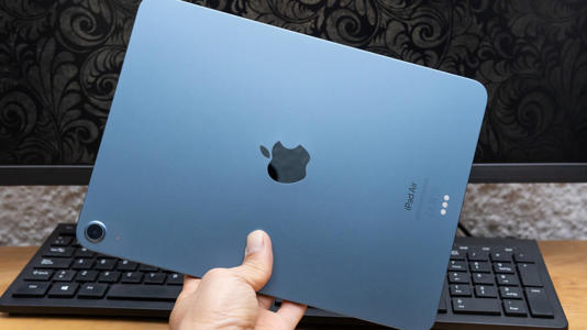 A hand holding an iPad over a desk and keyboard.