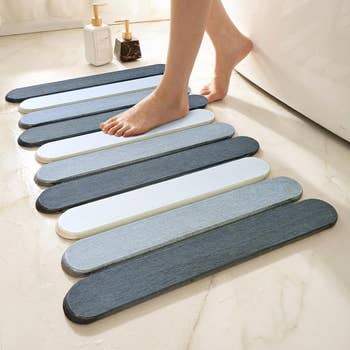 Person stepping onto a modern, absorbent bath mat beside a bathtub. Two pump bottles of bath products are in the background