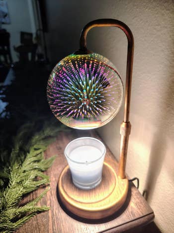 A decorative lamp with a spherical, light-reflecting design above a lit candle; pine branches are visible nearby on a wooden surface