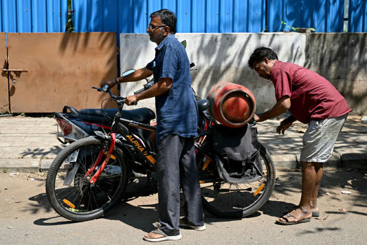 A man fastens a newly purchased LPG cylinder onto his cycle outside a gas agency in Chennai on 11 March (AFP via Getty)