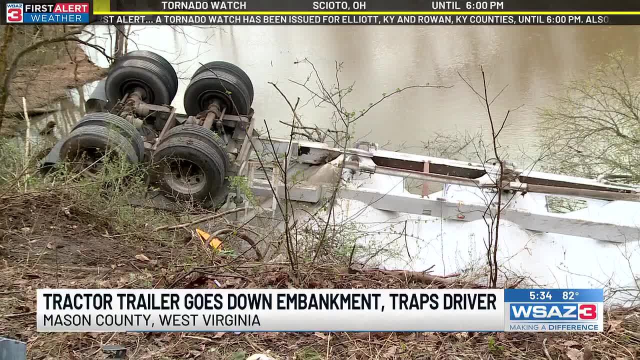 Truck driver charged after tractor-trailer rolls down embankment, traps ...