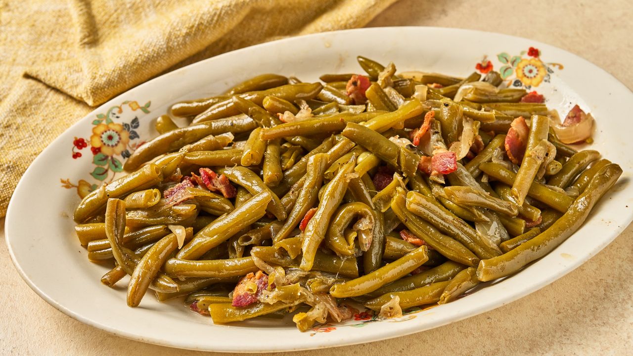 A platter of cooked green beans with pieces of bacon