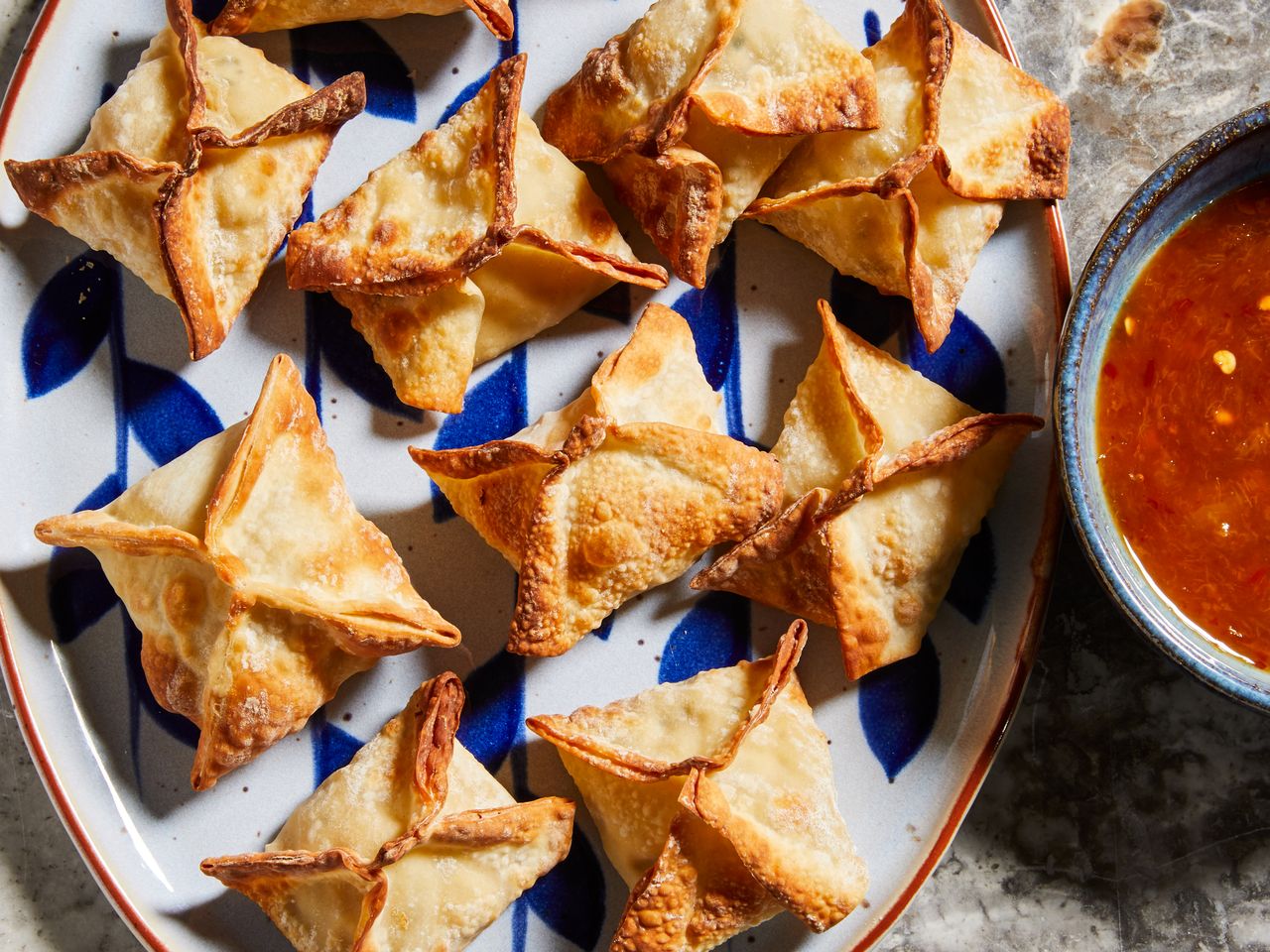 a close up, overhead view looking at a platter of golden-brown air fryer crab rangoon served with a sweet and sour dipping sauce.