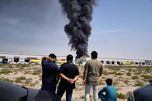 Residentes observan las llamas y una columna de humo se eleva desde un almacén en los Emiratos Árabes Unidos tras los informes de ataques iraníes en Dubai, 1 de marzo de 2026. AP Photo