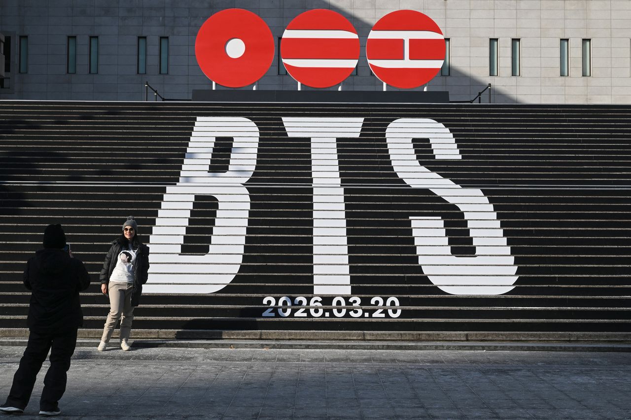 A woman poses for a photo in front of the stairs displayed with the logo of BTS' 2026 album and release date at Gwanghwamun Square in Seoul on January 14, 2026