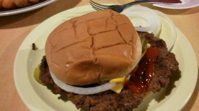 Giant burger patty on bun with onions, cheese, and ketchup on a white plate