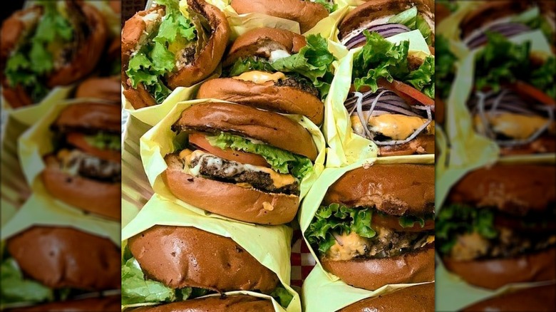 Hand holding a burger in a wrapper with cheese, onions, and lettuce