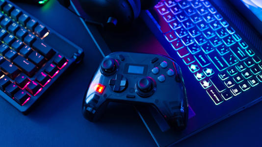 A PC gaming controller next to two keyboards, all bedecked in RGB.