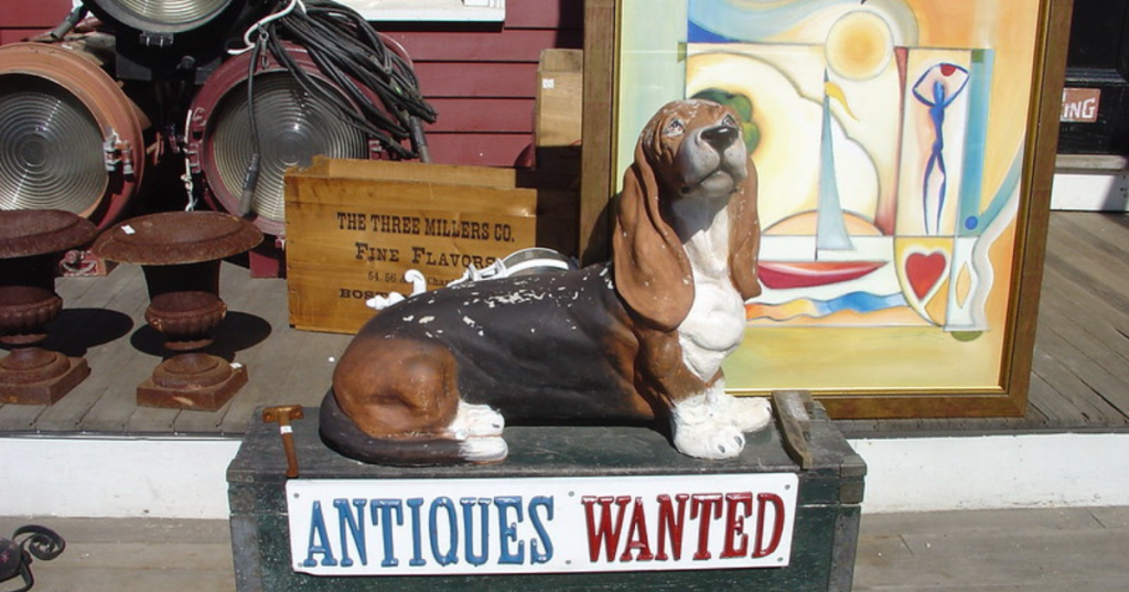 A statue of a basset hound sits on an old chest at the White Elephant antique store in Essex, MA. A sign on the chest reads