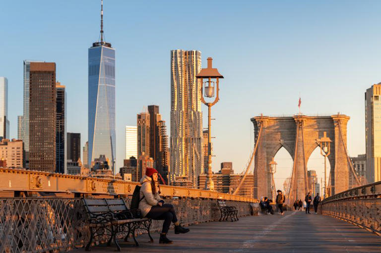 Beautiful woman sitting on a bench, smiling at the sun on Brooklyn Bridge, New York City