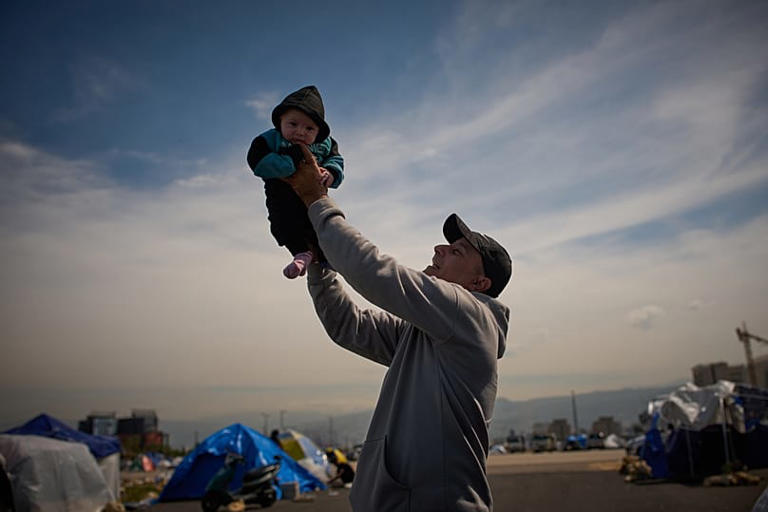 Un hombre desplazado de los suburbios de Dahiyeh, en el sur de Beirut, sostiene a su hijo de tres meses junto a una tienda de campaña utilizada como refugio en Beirut, Líbano, sábado 28 de marzo de 2026. Emilio Morenatti/Copyright 2026 The AP. All rights reserved.