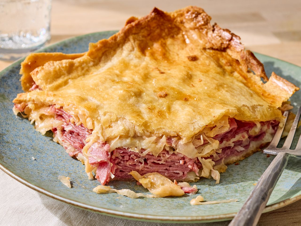 A slice of a baked dish resembling a Reuben crescent pie on a plate with a fork