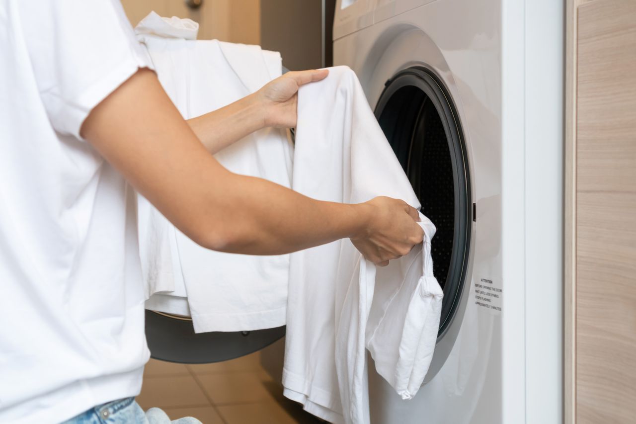 Hands of woman loading white color clothes into washing machine at home. Close up. Laundry concept.