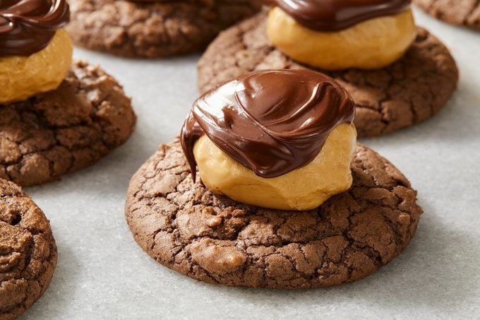 Chocolate cookies topped with a dollop of peanut butter and drizzled with melted chocolate, arranged on parchment paper.