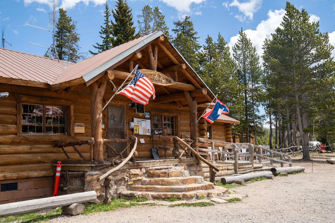 A log cabin store with American and state flags displayed located in a wooded area
