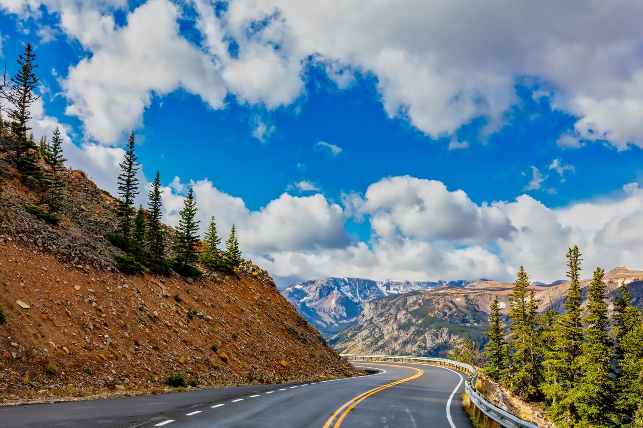 A scenic highway winding through a mountainous landscape bordered by trees and rocky hills