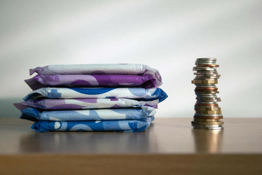 A stack of sanitary towels next to a taller stack of coins. Illustrating period poverty and unaffordability of sanitary materials for many women world