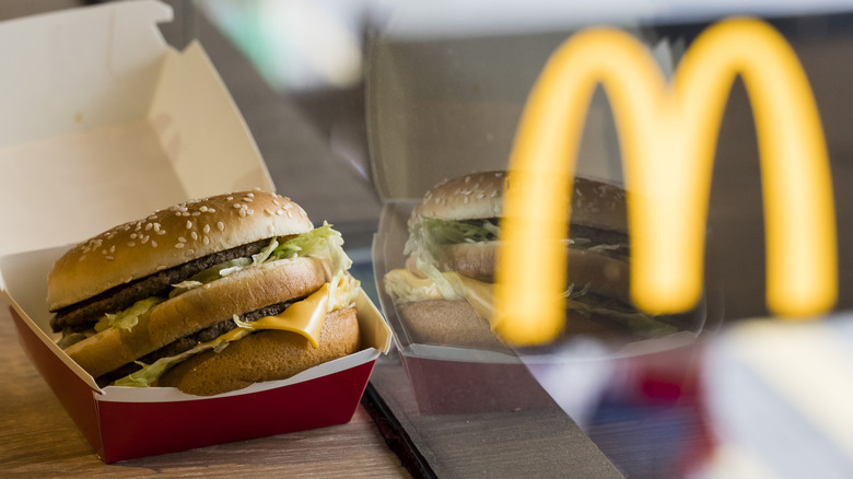 Big Mac in its box with McDonald's Golden Arches reflected in the window beside it