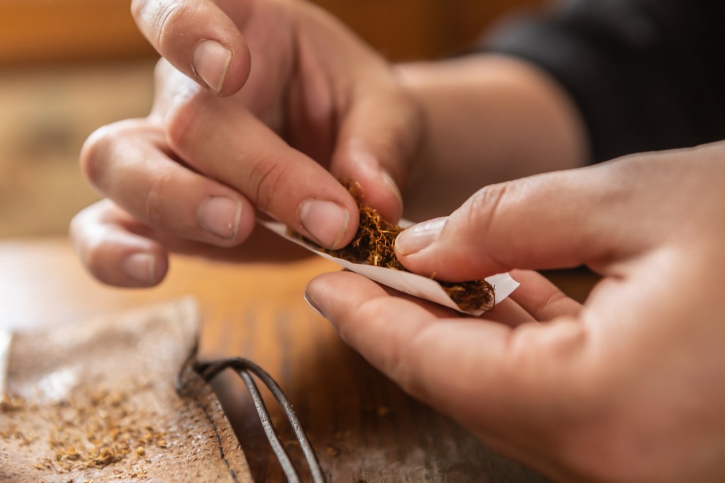 a person rolls a cigarette with tobacco