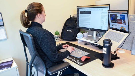 A person sitting at a desk writing for How To Geek with a laptop and an external monitor.