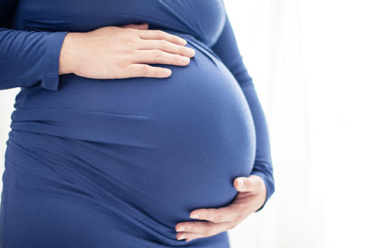 Pregnant woman in blue dress holds her belly bump. Bright photo on white background