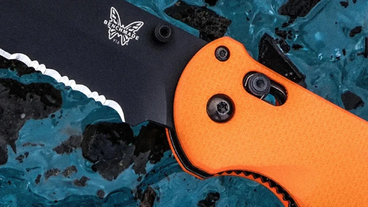 Black partially serrated Benchmade 916 knife blade with orange textured handle on a blue and black surface.