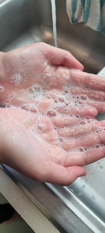 Hands covered in soap bubbles under running water near a sink