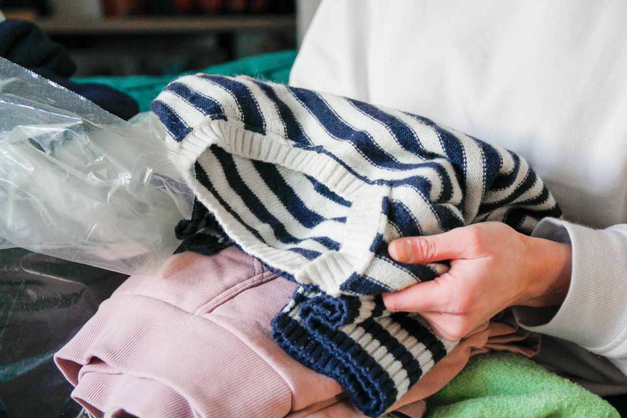 Person folding clothes focusing on their hands and a striped sweater
