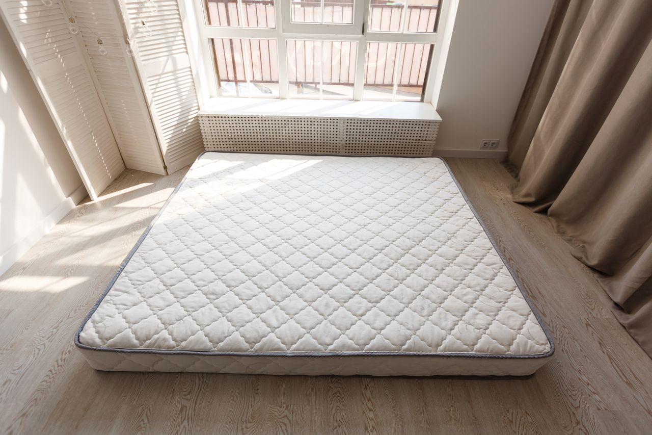 A mattress on the floor of a room with sunlight streaming in through the window