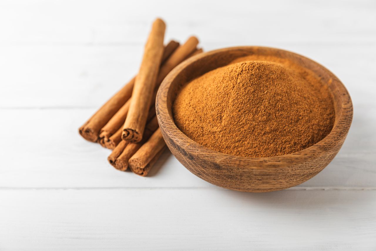 A wooden bowl filled with ground cinnamon positioned beside several whole cinnamon sticks
