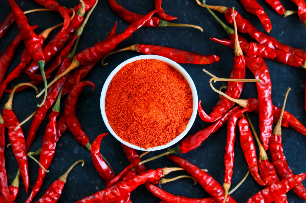 A bowl of ground red pepper surrounded by whole red chili peppers
