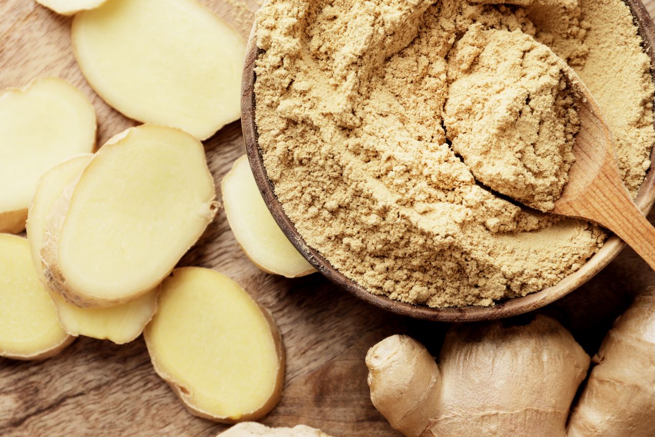 Slices of fresh ginger and a wooden bowl of powdered ginger with a spoon