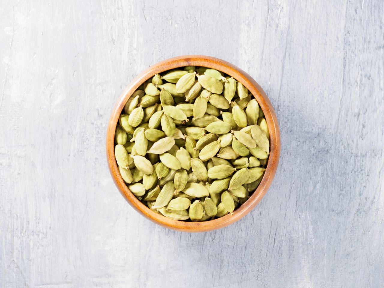 A bowl of cardamom pods on a gray surface