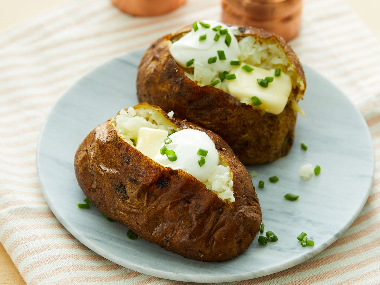 close up on two air fryer baked potatoes topped with butter, sour cream and chives
