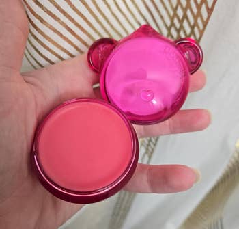 Round pink lip balm in a hand with a playful, bear-shaped pink case
