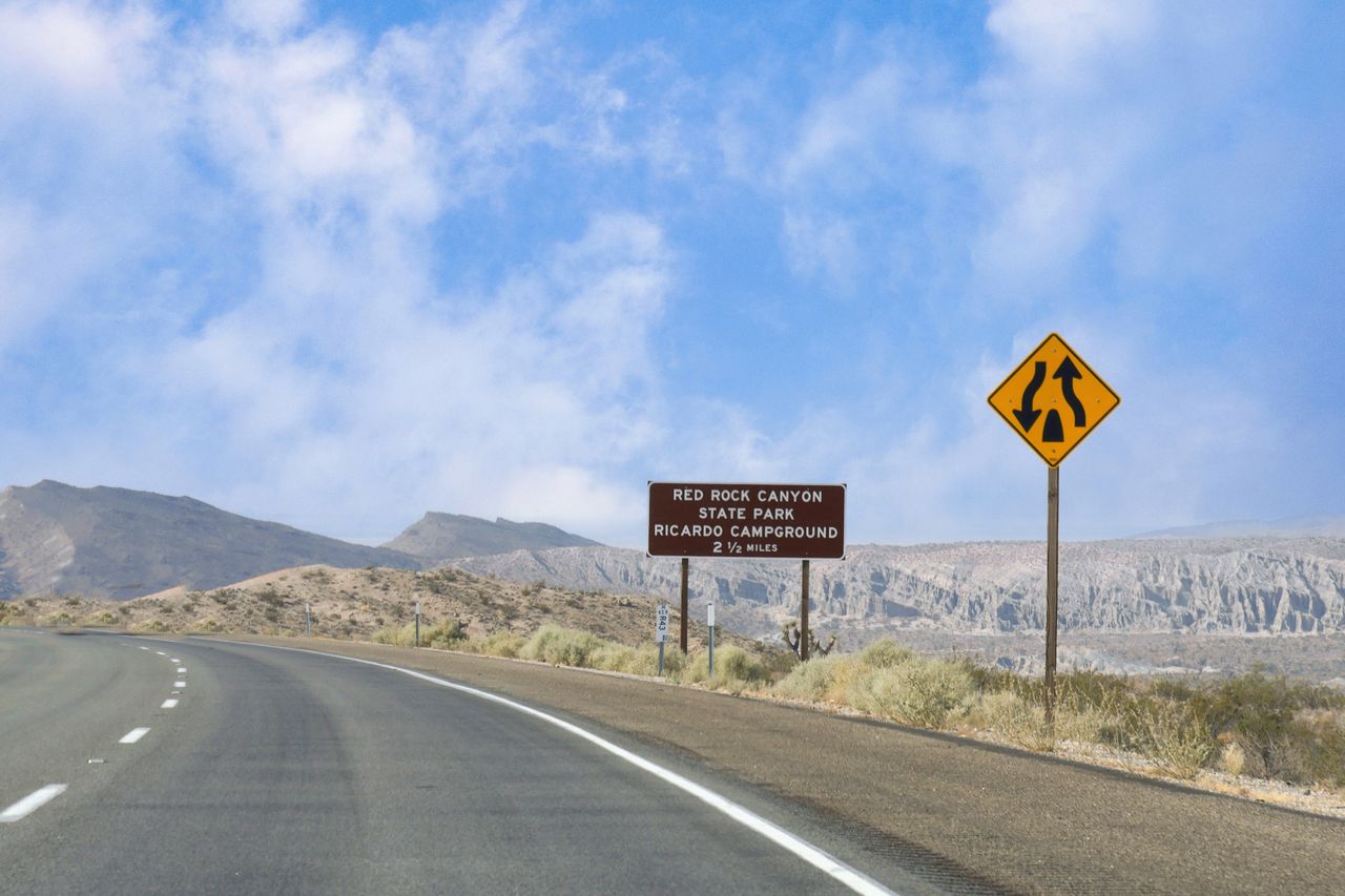 Road sign for Red Rock Canyon State Park and Ricardo Campground with merging traffic sign and desert landscape