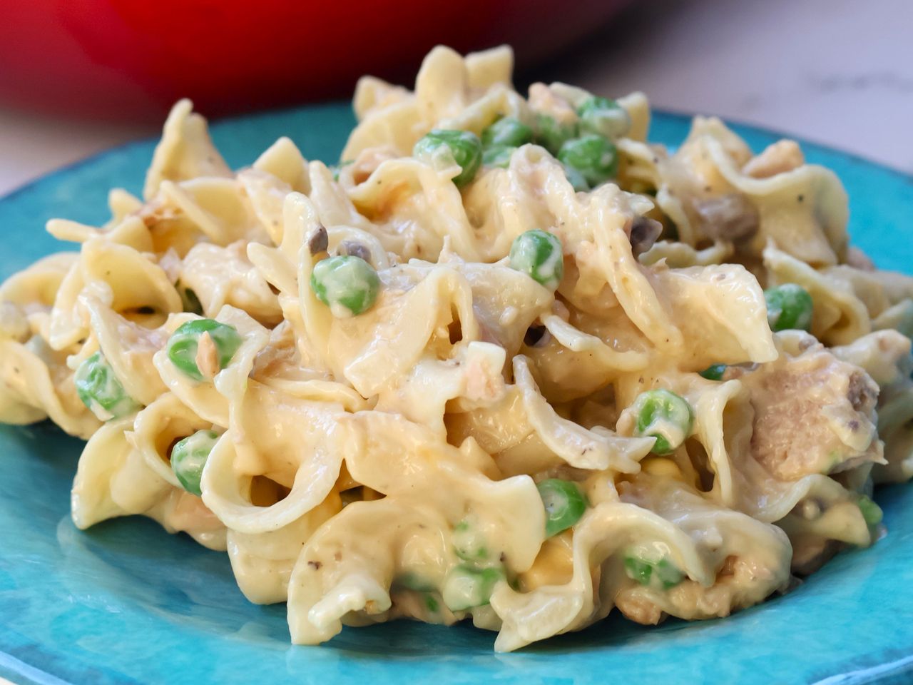 a serving of Quick and Easy Tuna Casserole on a blue glazed plate with a red pot in the background