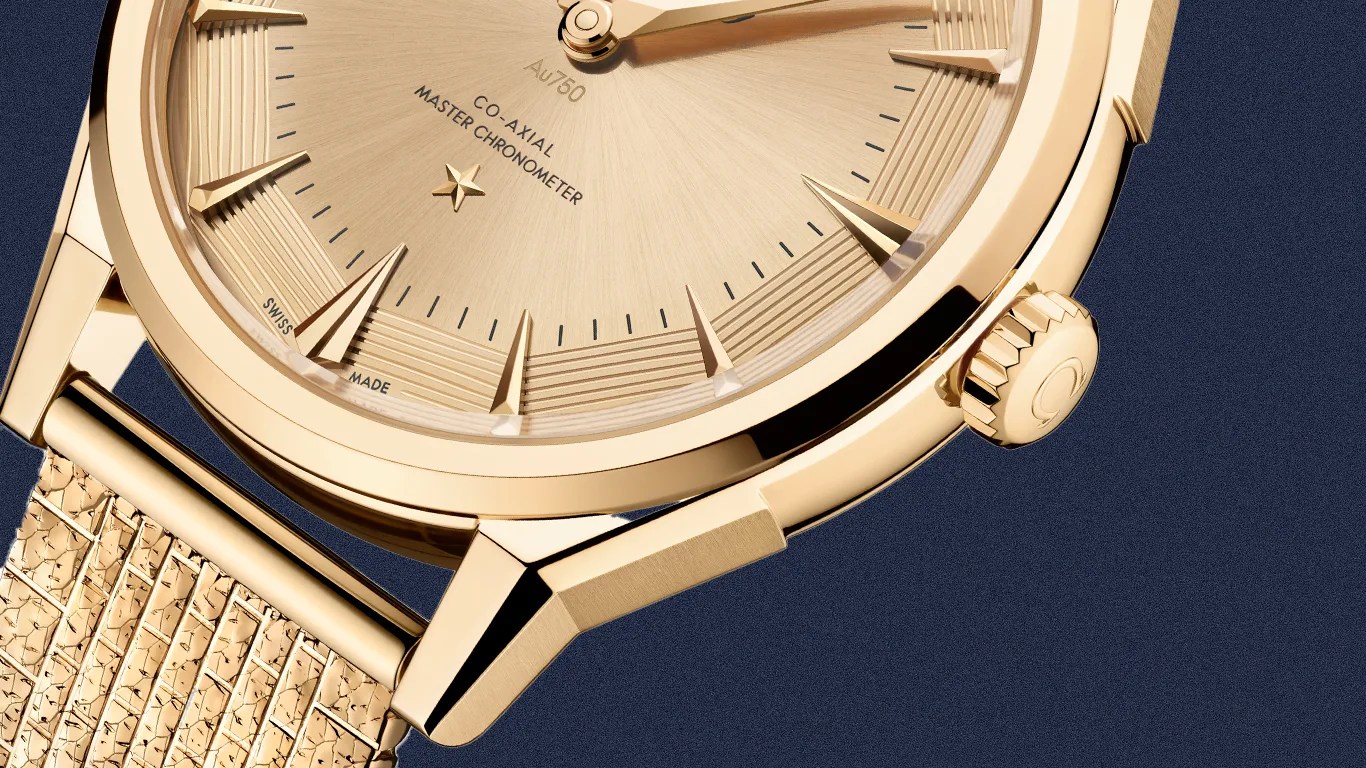 Close-up of a gold wristwatch with a textured gold dial, triangular hour markers, and a gold mesh strap.