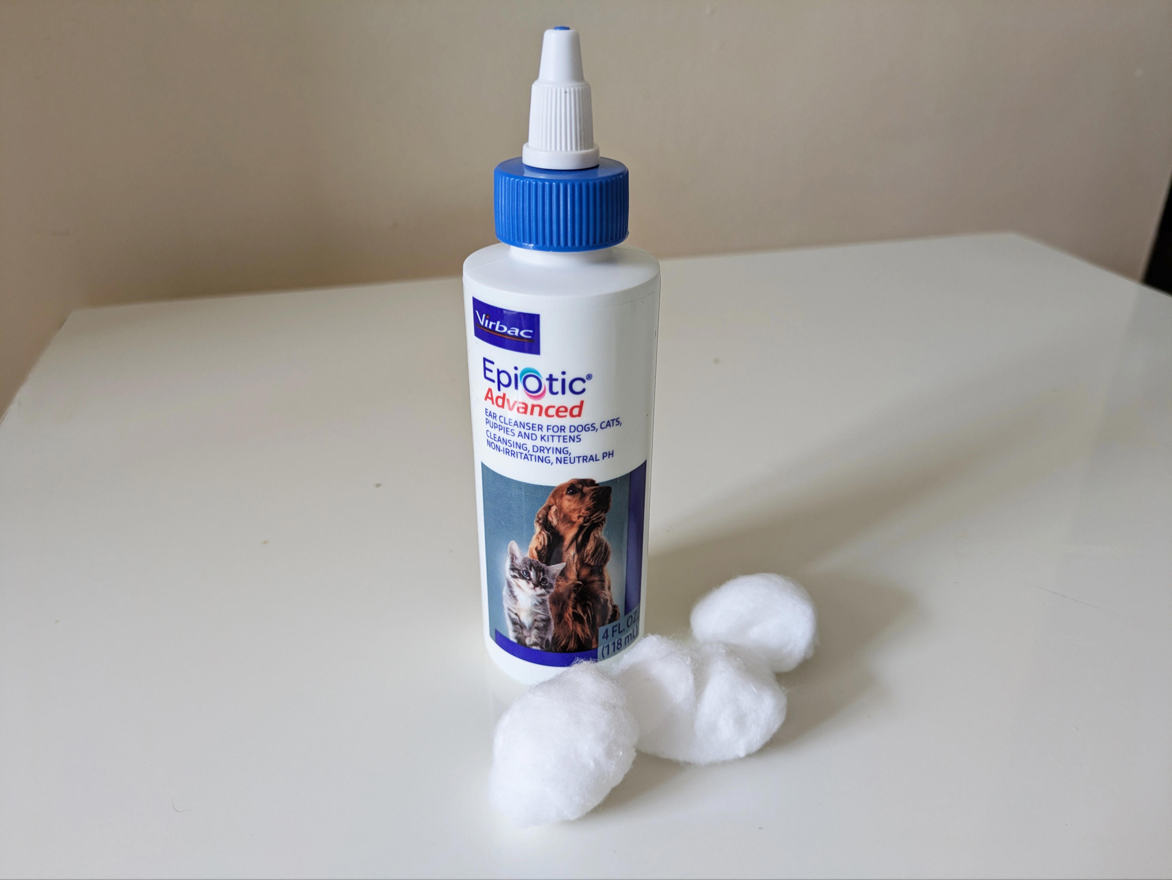 A bottle of Virbac Epiotic Advanced pet ear-cleaning solution sits on a white table next to several cotton balls.