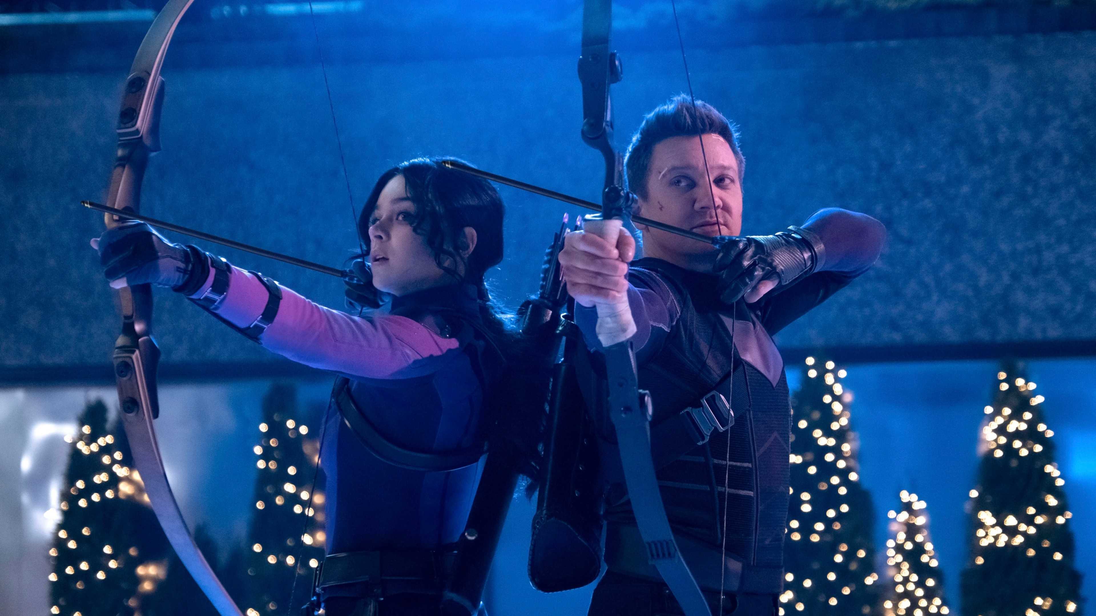 Hailee Steinfeld as Kate Bishop and Jeremy Renner as Clint Barton Holding bows and arrows on an ice rink in Hawkeye