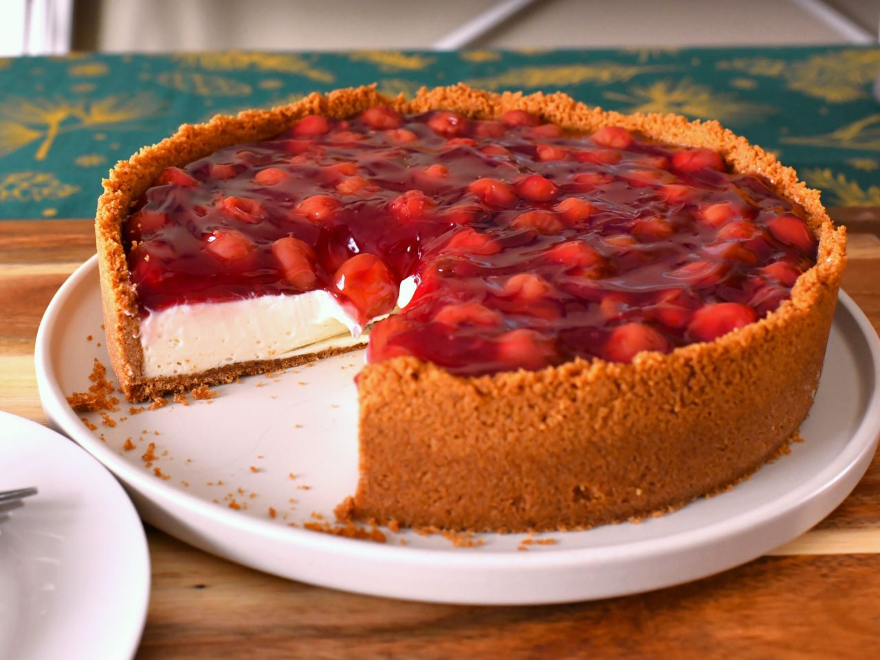 whole cream cheese pie with cherry topping in graham cracker crust and one slice removed